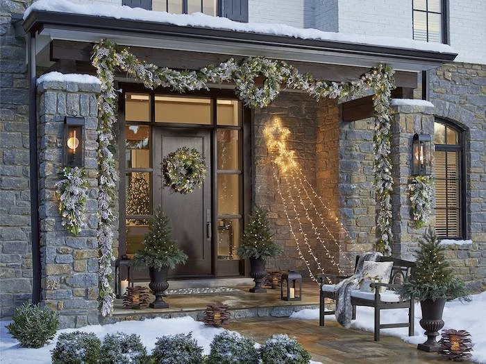 wreaths hanging on the door and door frame, outdoor lighted christmas decorations, strings of lights hanging from the wall to a bench