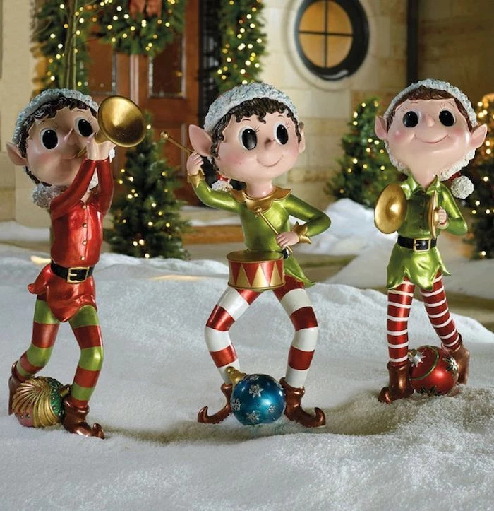 three elf figurines, placed in the snow in front of a house, diy outdoor christmas decorations, door decorated with wreaths with lights