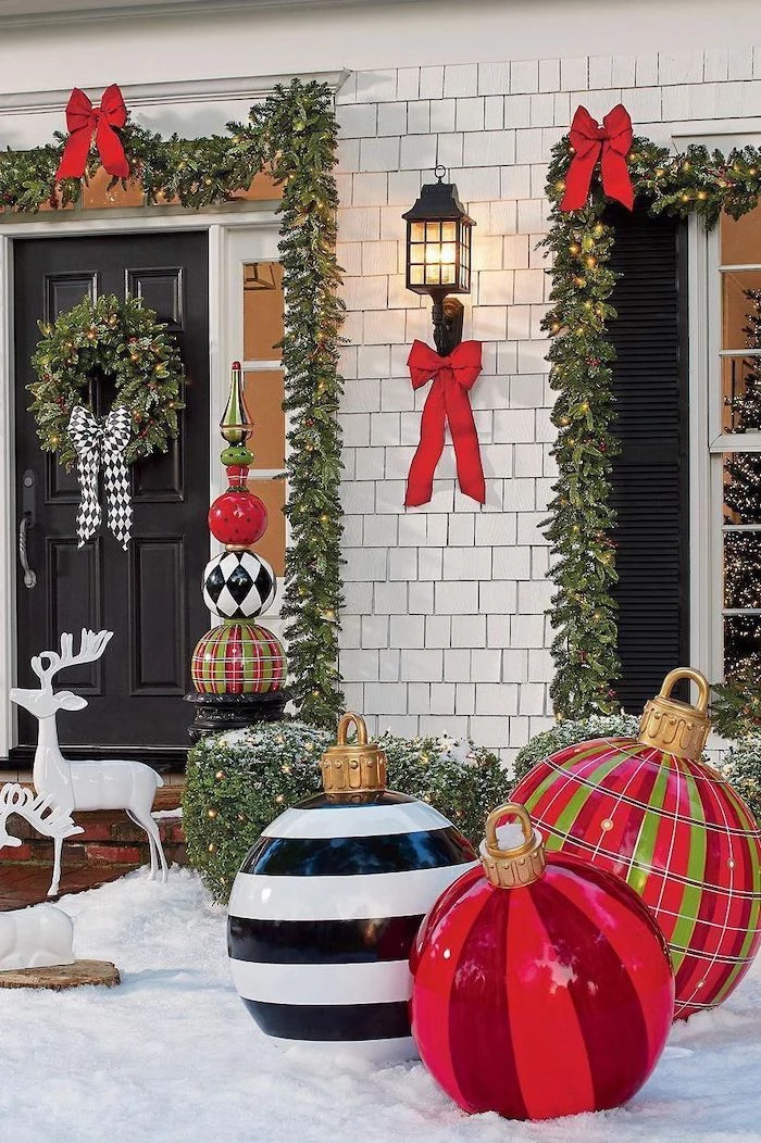 wreaths with red ribbons, hanging over the door and window frames, outdoor lighted christmas decorations, large baubles in the snow