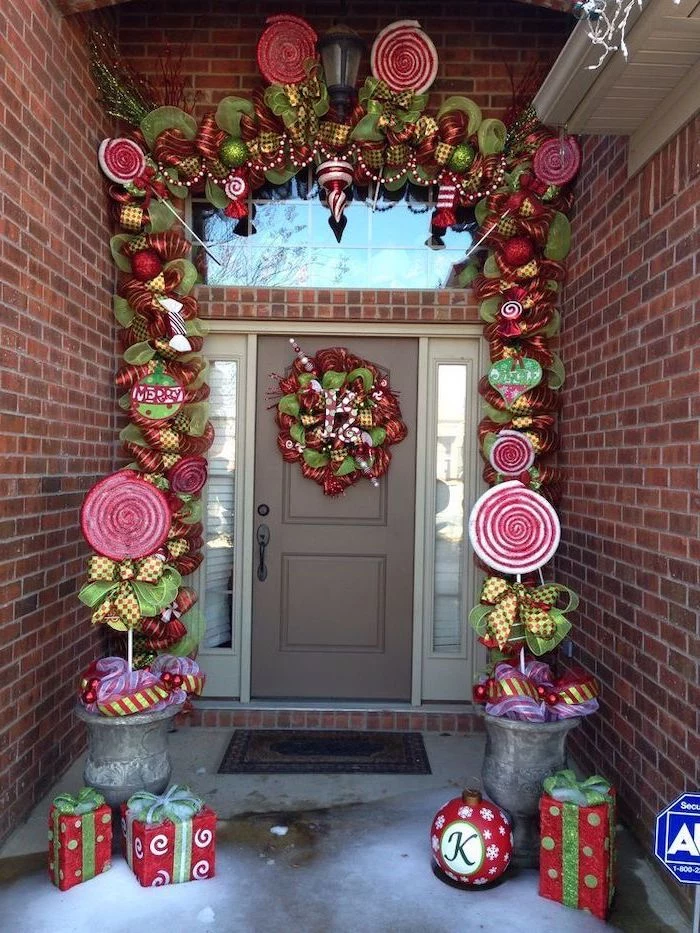 wreath made of green and red ribbons, hanging on door and door frame, outdoor lighted nativity scene, wrapped presents on both sides