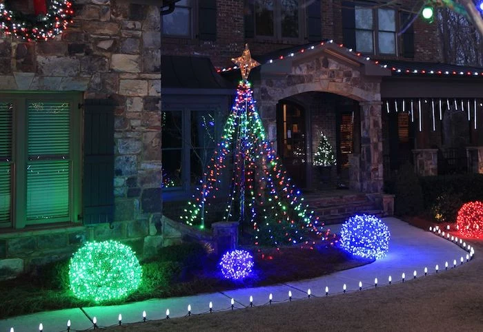 lights along a pathway, leading to a house, bushes on the side, decorated with lights in blue and green, outdoor lighted nativity scene