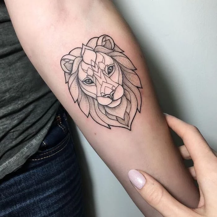 lion head with mane, geometrical design, on woman wearing jeans and dark grey top, lion king tattoo, forearm tattoo