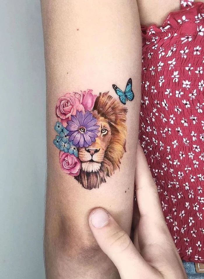 back of arm tattoo, lion tattoo meaning, lion head with colorful flowers surrounding it, blue butterfly in the corner