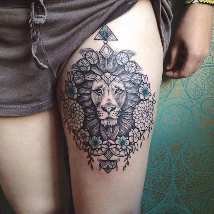 thigh tattoo, mandala tattoo, lion tattoo on arm, lion head with large mane, blue flowers around it, mandala flowers