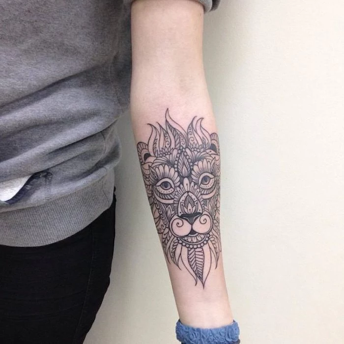 tribal lion tattoo, mandala lion forearm tattoo, on woman wearing grey blouse and black jeans