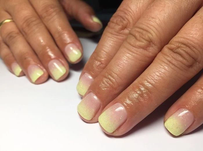 nude to yellow gradient glitter nail polish, ombre coffin nails, short squoval nails, hands placed on white surface
