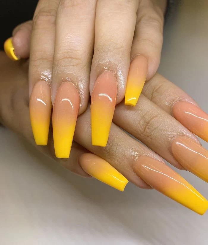 nude to yellow gradient nail polish, ombre nail designs, extra long coffin nails, hands placed on white surface