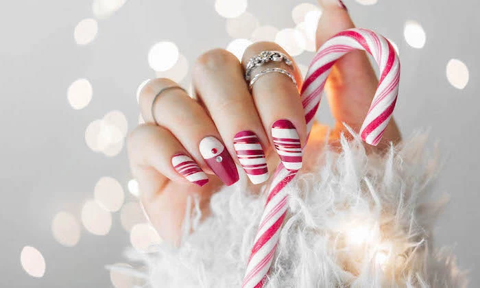 red and white nail polish, candy cane decorations on each nail, christmas nail colors, hand holding a candy cane
