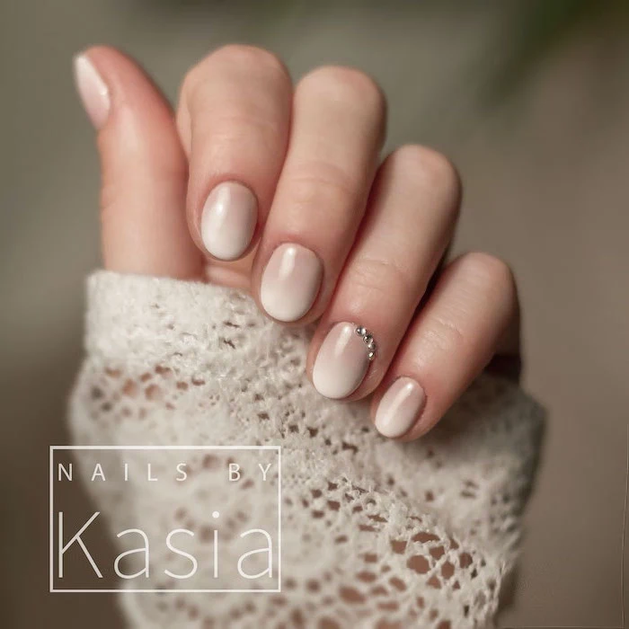 short squoval nails, nude to white gradient nail polish, rhinestones decorations on the ring finger, french ombre nails