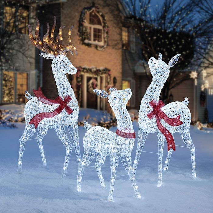 three reindeer figurines with lights, decorated with red ribbons, placed in the snow, outdoor snowman decoration