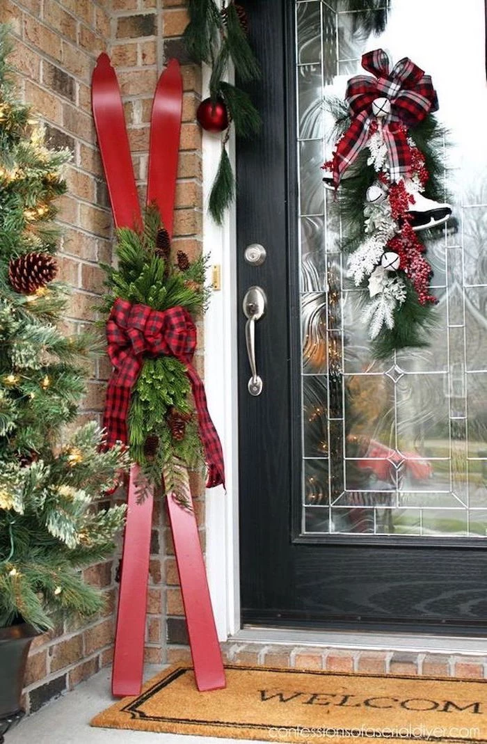 two red skis decorated with tree branches and plaid ribbon, outdoor snowman decoration, placed on the side of a door