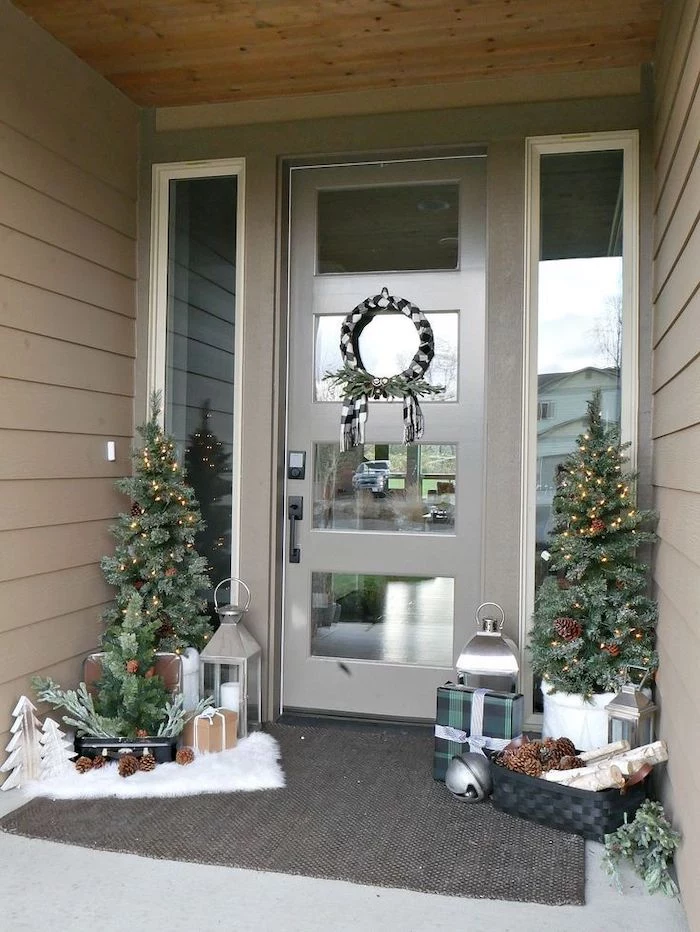 outside christmas decoration ideas, two trees with lights, placed on both sides of a door, decorated with wreath, made of black and white ribbons