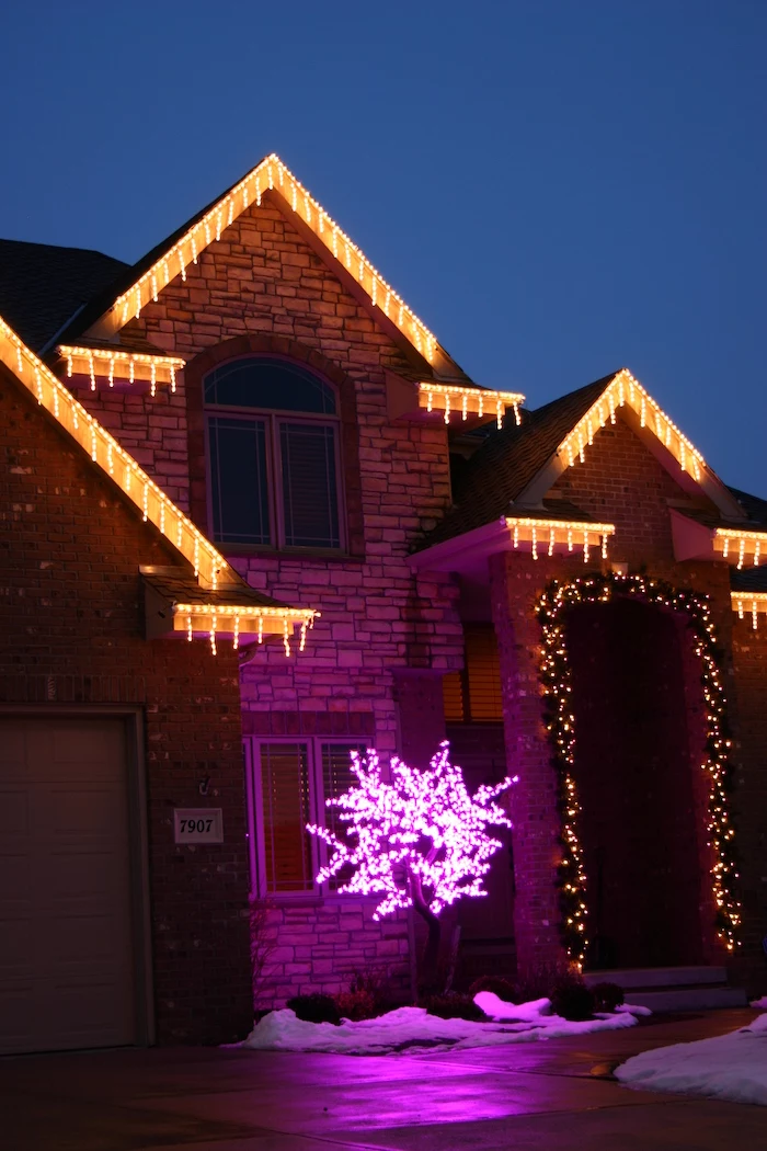 two storey house, decorated with lights, outside christmas decoration ideas, wreath with lights on the door frame, tree with pink lights