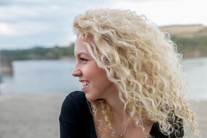 woman smiling, medium length very curly blonde hair, winter hair colors, wearing black blouse