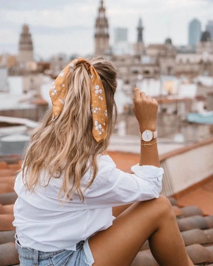 woman sitting on a roof, overlooking the city, wearing white shirt and denim shorts, winter hair colors, blonde hair with highlights