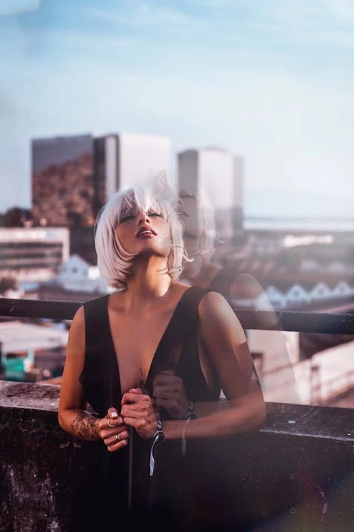 woman wearing black dress, hair color for short hair, standing on a balcony, short straight bob with bangs, ash grey hair