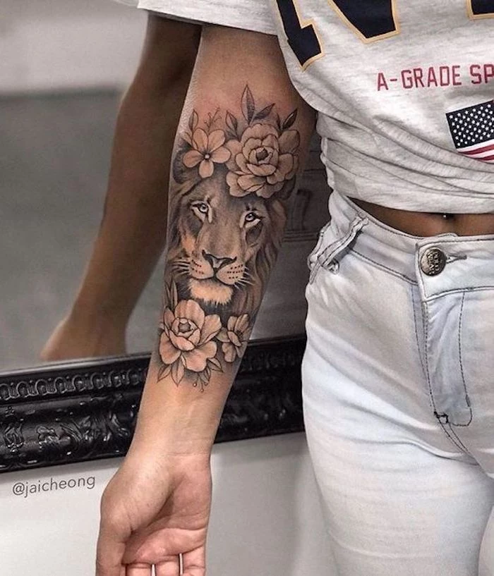 woman wearing white jeans and grey t shirt, small lion tattoo, forearm tattoo, lion head surrounded by flowers