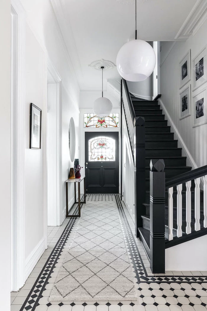 hallway with black and white tiled floor, stained glass windows, black door with windows, black staircase and white walls