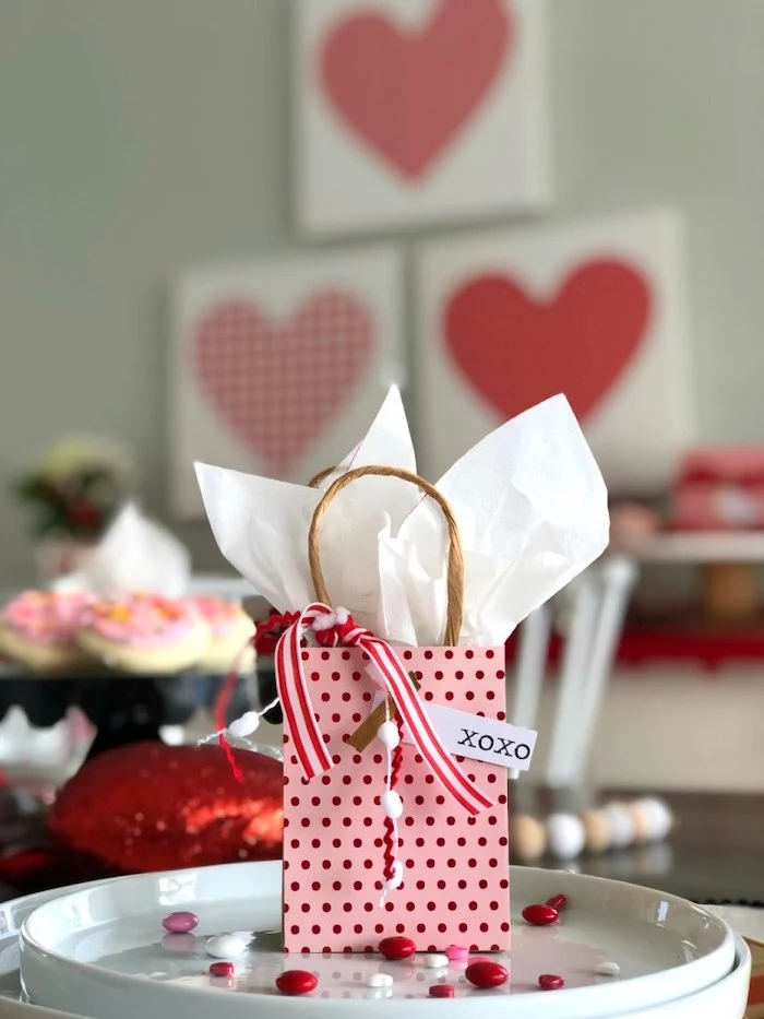 small paper bag, filled with candy, placed on white plate, valentine decorations, red and white candy scattered on it