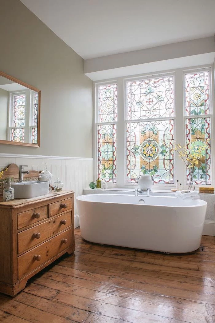 bathroom with wooden floors, bathtub under the window, stained glass windows, wooden cabinet under the sink