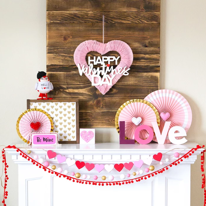 valentines day decor, pink and red decorations, heart garlands hanging over white mantel, decorations made of paper