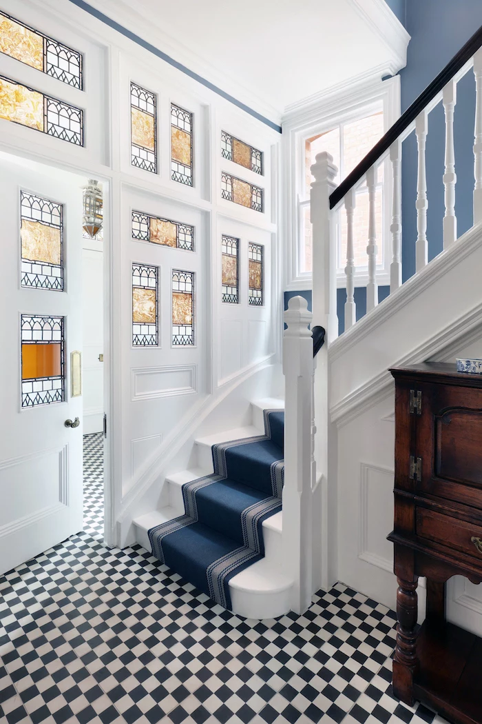 white staircase with blue carpet, stained glass panels, white and black tiled floor, large door with decorated windows