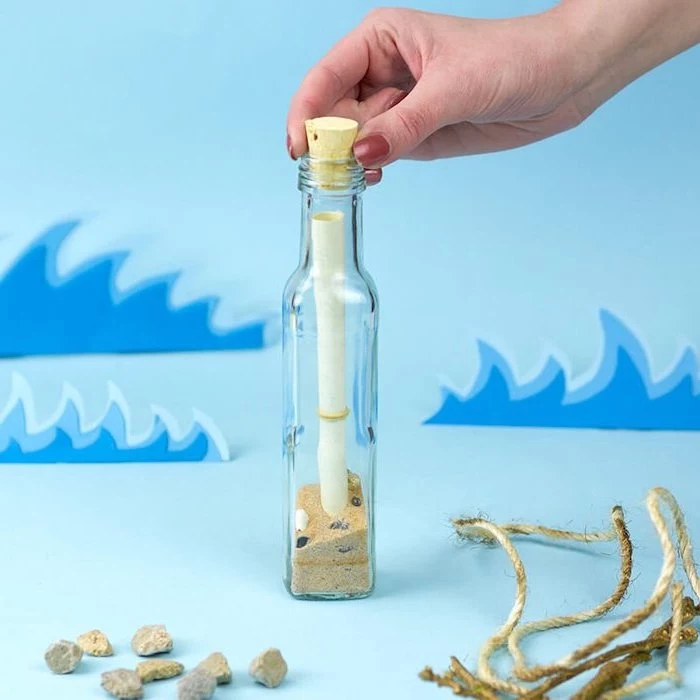 message in a bottle, bottle with sand and stones inside, cork on top, valentines gifts for her, placed on blue surface