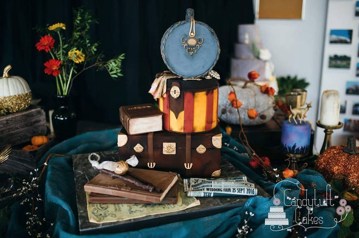 large cake with multiple different layers, shaped as trunks and books, arranged on large tray, happee birthdae harry