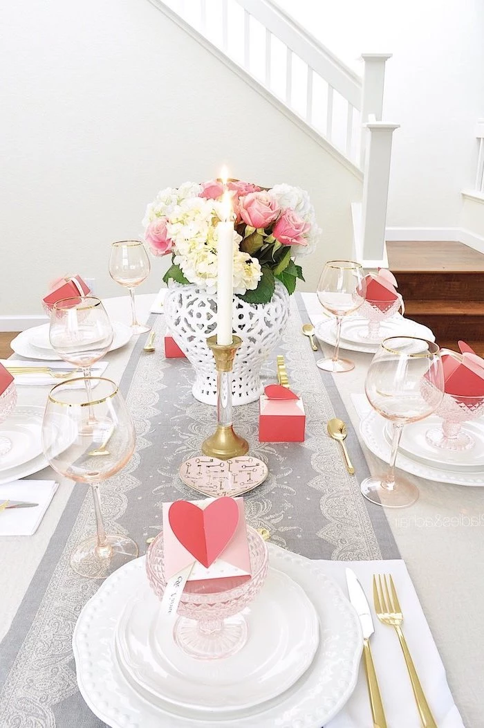 dinner table with candles, heart decorations, flower bouquet in the middle, pink heart boxes inside glasses