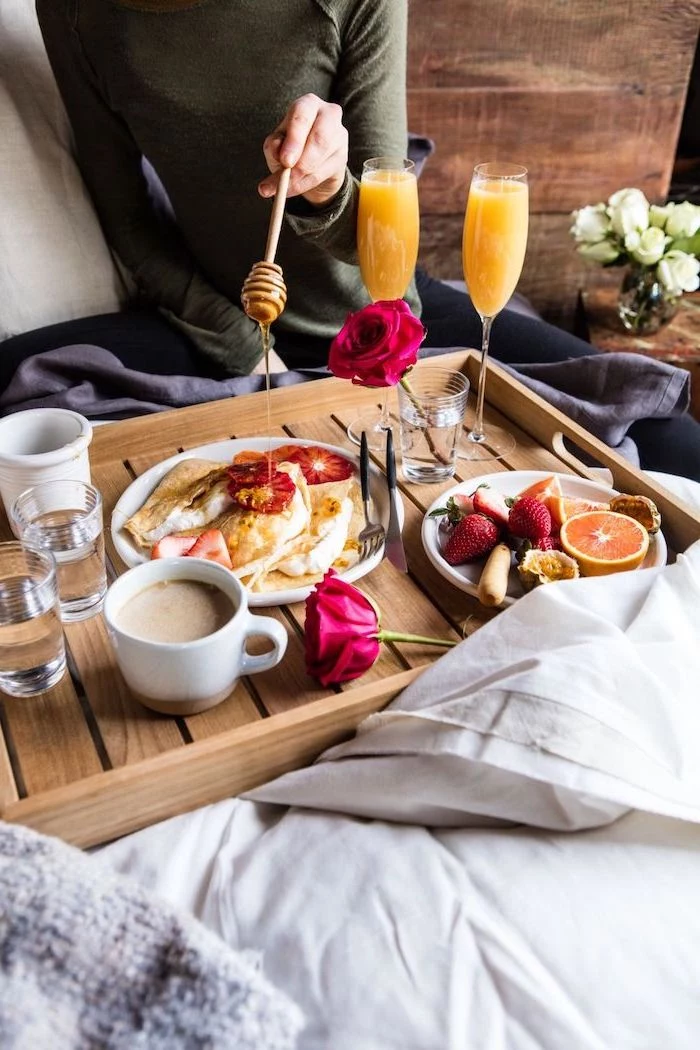 breakfast in bed, served on wooden tray, valentines day ideas for her, pancakes and fruits in white plates, orange juice and coffee