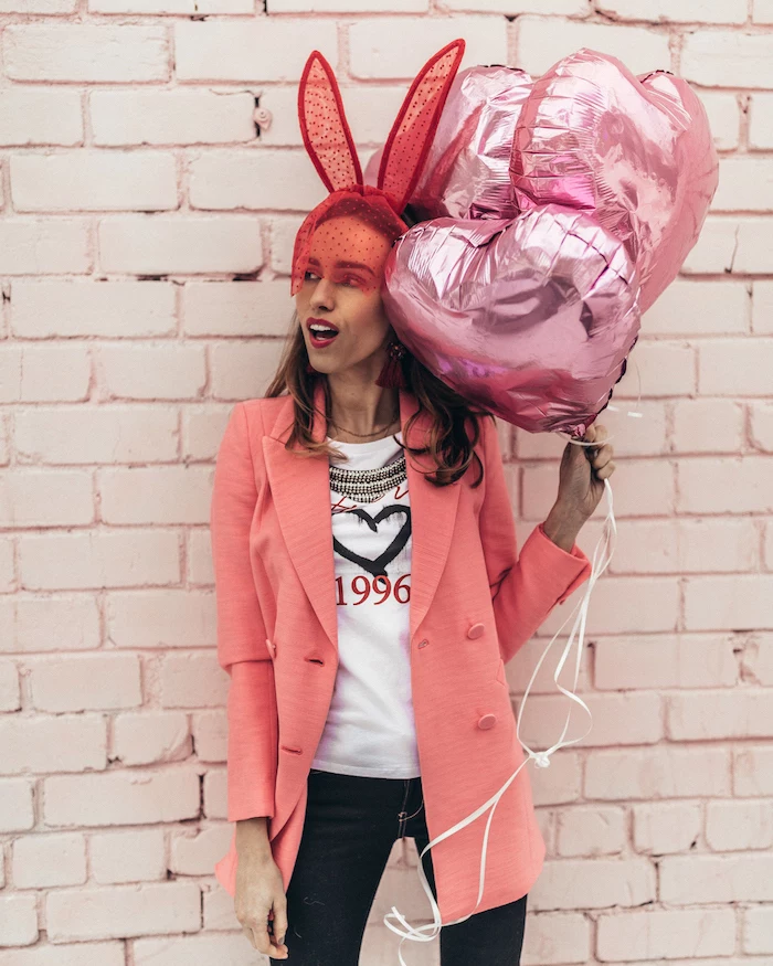woman holding a bunch of pink, heart shaped balloons, valentines dress, wearing white t shirt and jeans, pink blazer