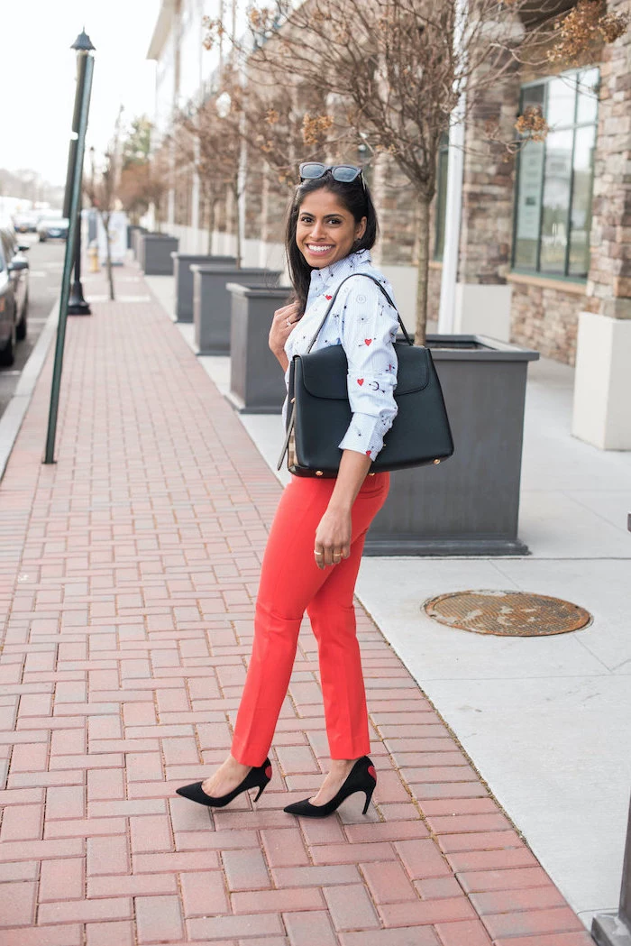 woman walking on the sidewalk, wearing red pants, blue shirt and sunglasses, black bag and shoes, valentines dress