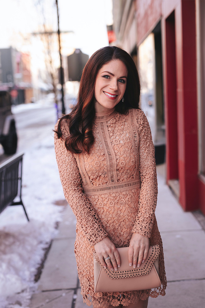 brunette woman smiling, wearing nude lace dress, valentines outfits, holding nude leather clutch