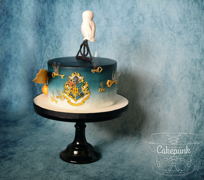 cake covered with blue and white fondant, placed on black cake stand, happee birthdae, deathly hallows symbol and hedwig on top