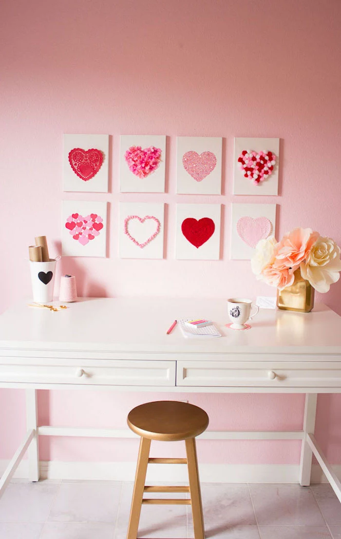 valentine decorations, eight canvases with different hearts portrayed on them, hanging on pink wall, over a white desk