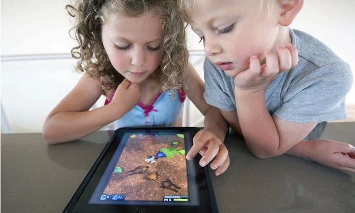 children's games, little boy and girl leaning on a grey surface, playing games on a tablet