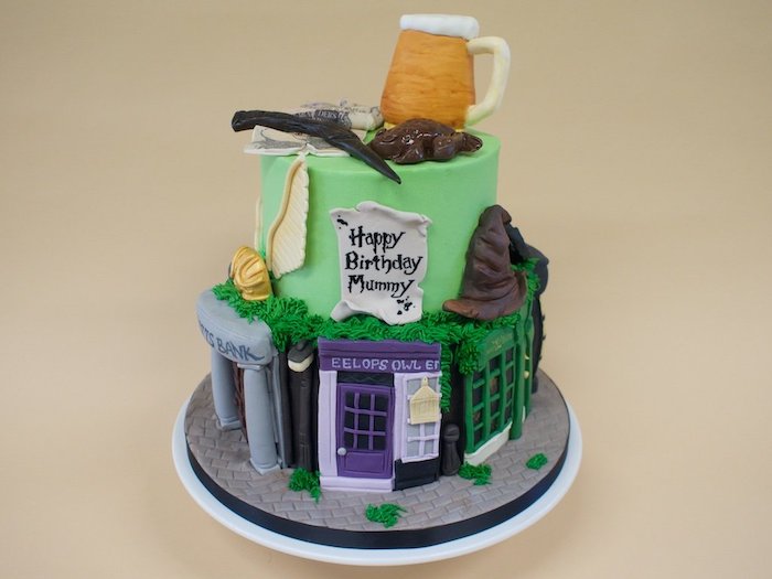 two tier cake with green fondant, diagon alley shops on the bottom tier, harry potter cake hagrid, butterbeer on top