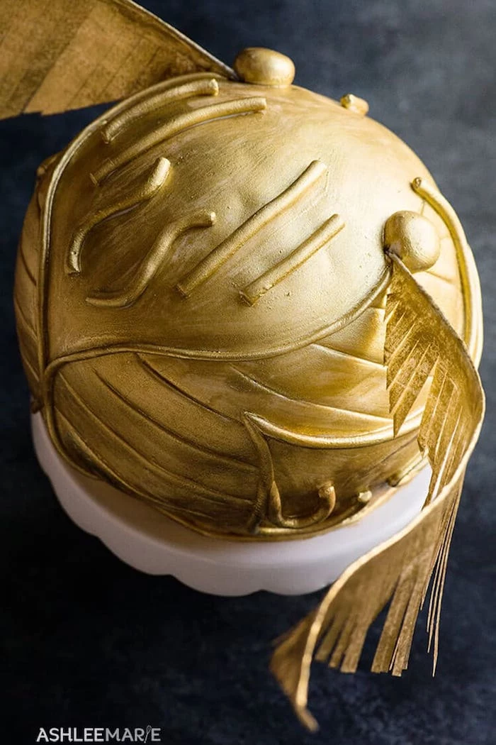 golden snitch cake, placed on white cake stand, harry potter cake, step by step diy tutorial