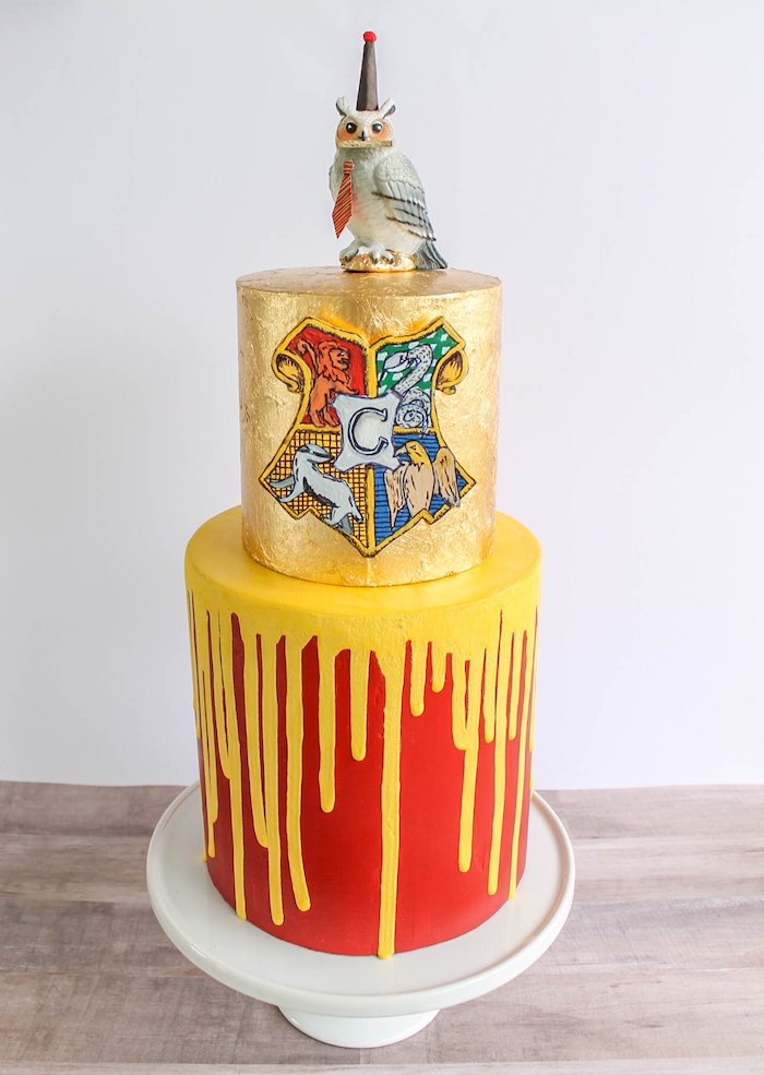 two tier cake, one gold tier with hogwarts symbol, hagrid cake, bottom gryffindor tier with red and yellow fondant