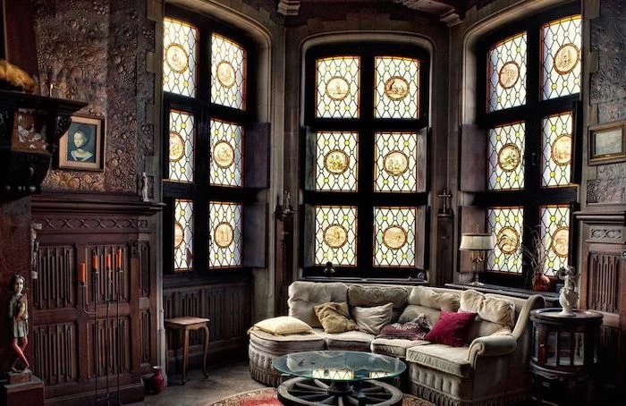 large windows in gothic style living room, grey sofa with throw pillows, stained glass doors, wooden fireplace