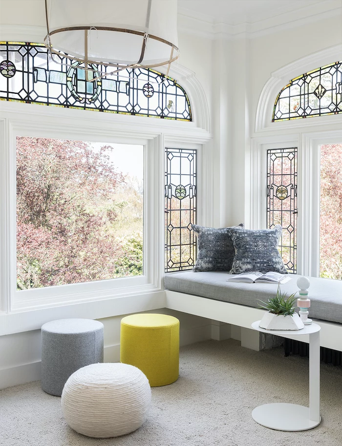 large windows, how to make stained glass, grey white and yellow ottomans, next to bench with grey throw pillows