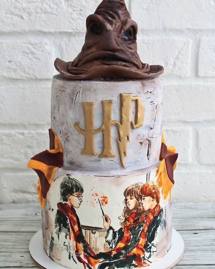 two tier cake with white fondant, harry potter themed cake, sorting hat on top, harry ron and hermione painted on the bottom tier