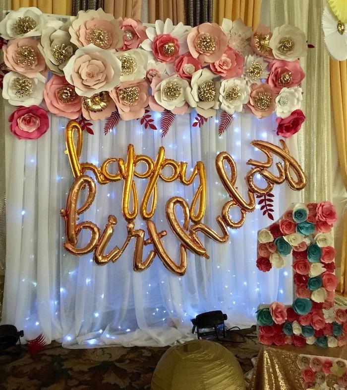 happy birthday balloons, hanging on white tulle with fairy lights, crepe paper flowers, paper flowers arranged on top