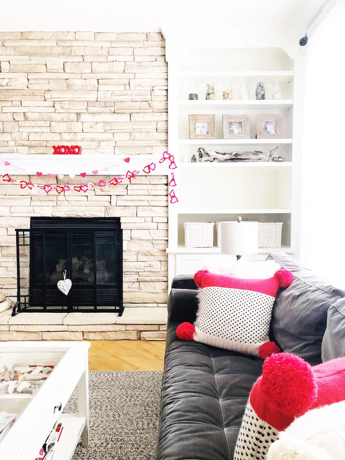 valentines day decor ideas, hearts garland hanging over mantel, pink and white throw pillows with black hearts, black velvet sofa