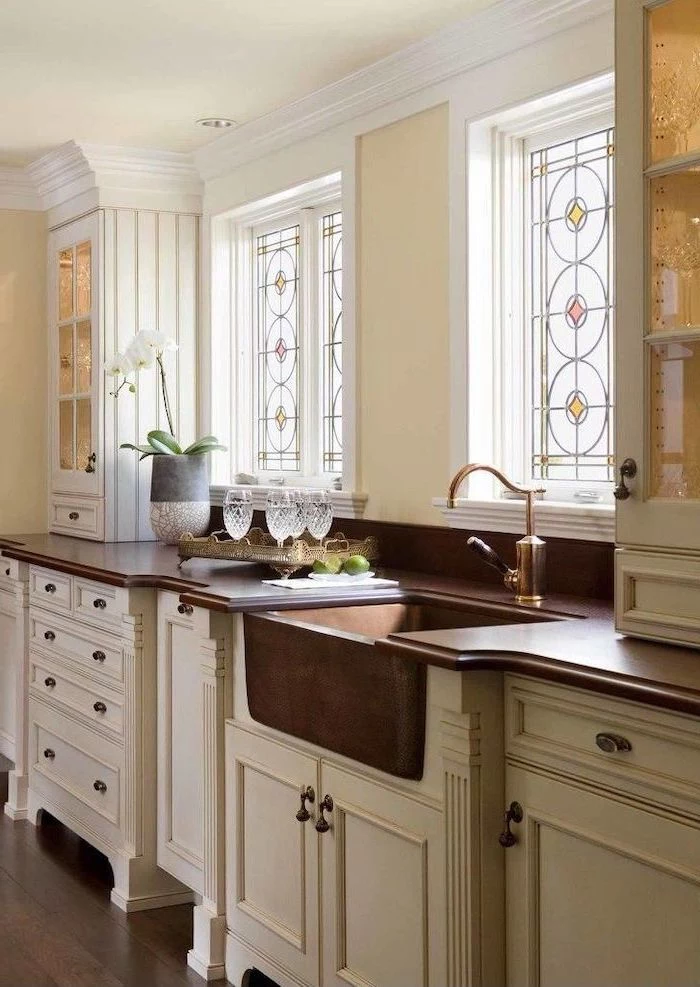 stained glass window hangings, kitchen with white cupboards, dark wooden countertops, large windows