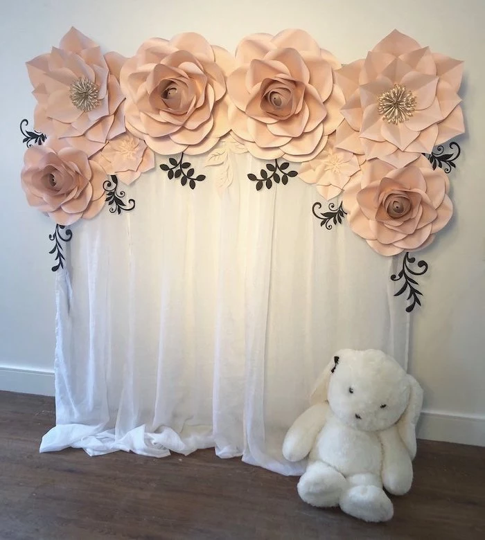 large blush flowers hanging on the wall, on top of white tulle, paper flower wall decor, hanging on white wall, plush bunny on the floor