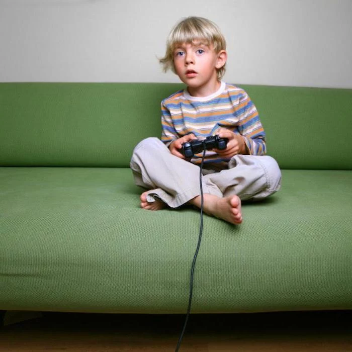 little boy with blonde hair, sitting on green sofa, children's games, playing video games