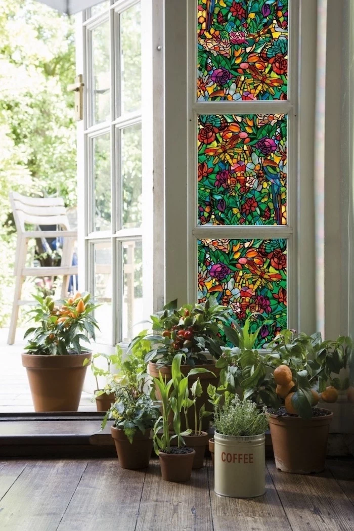 lots of potted plants in different pots, arranged on wooden floor, stained glass window hangings, placed in front of a door