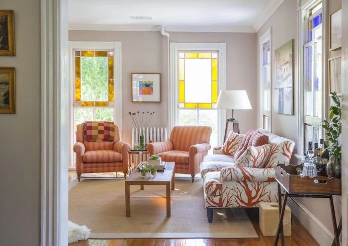 orange armchairs and white sofa in living room, large windows and wooden floors, stained glass window hangings, wooden coffee table