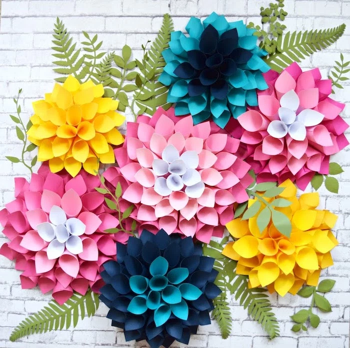 paper flowers in different colors, arranged together on white brick wall, how to make flowers out of tissue paper